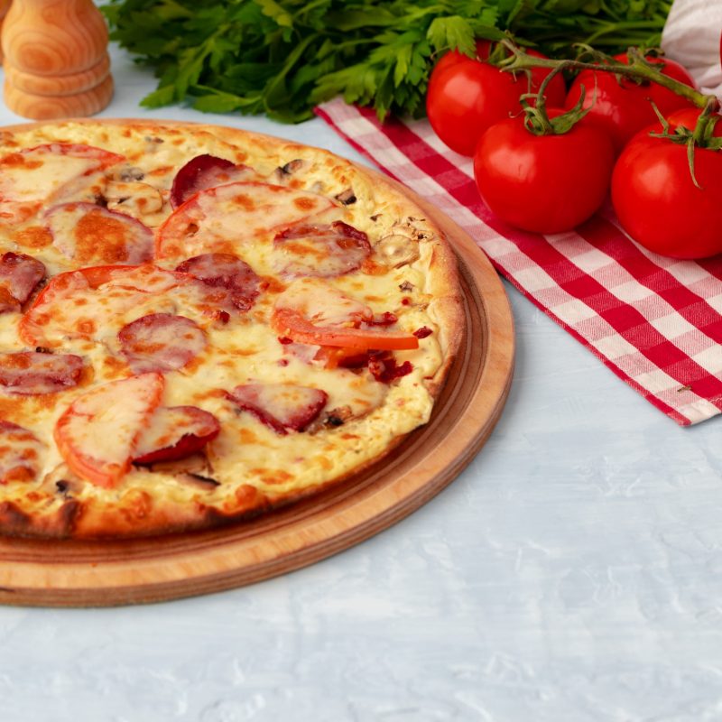 Färsk pizza på bord intill tomater och grönsaker